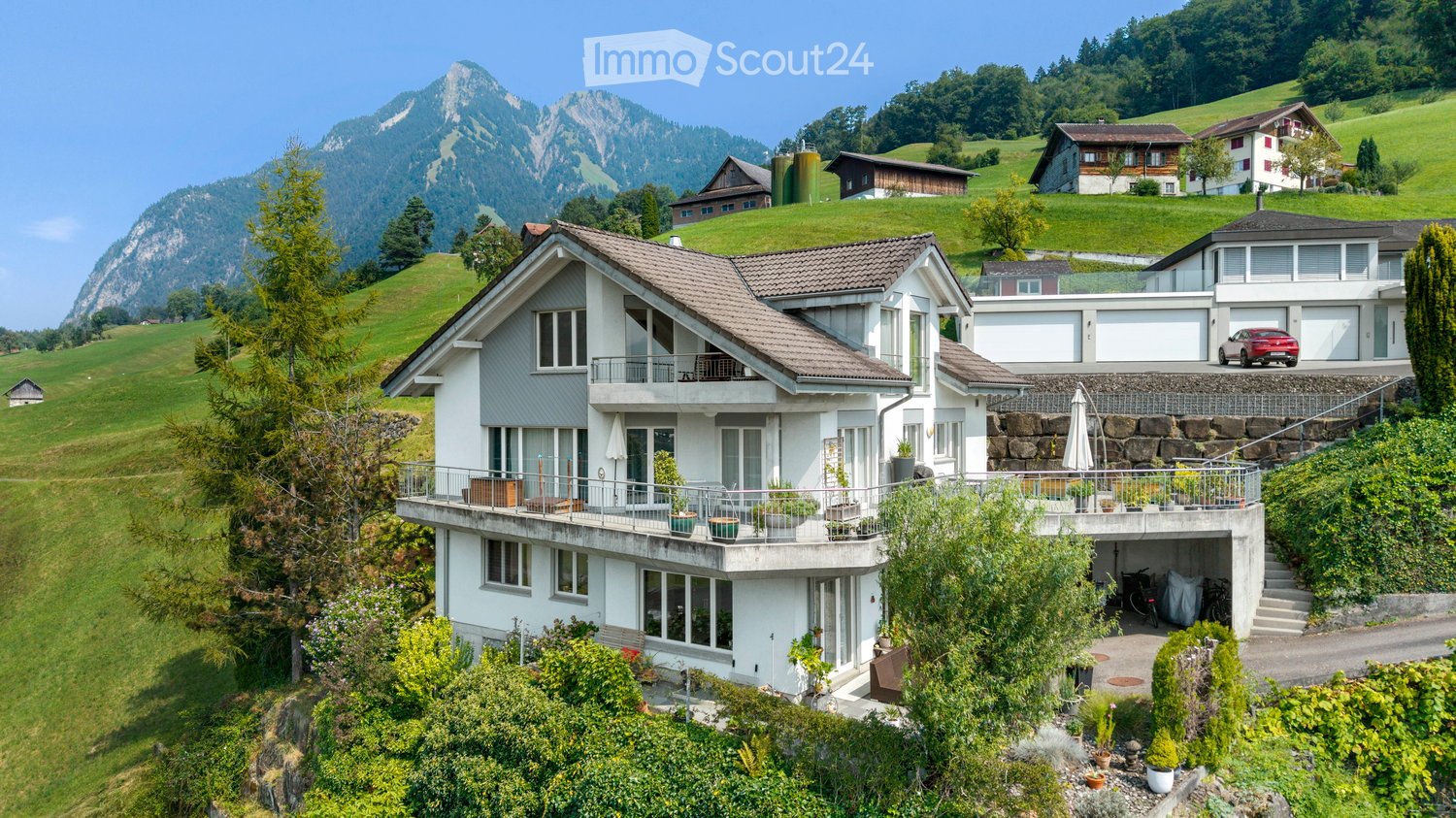 3 story white house, brown roof, multiple windows, 2 balconies, 2 cars parked, stairs to enter the house