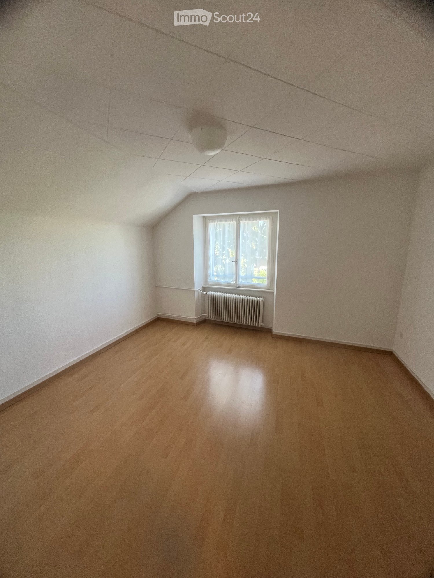 Empty room with wooden floor, white walls, radiator, window, ceiling light