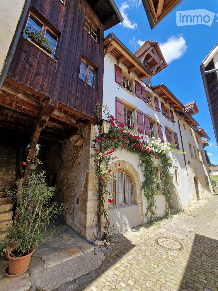 Cobblestone pathway, white building with wooden balcony, red shutters, blooming flowers, stone wall, brick structure