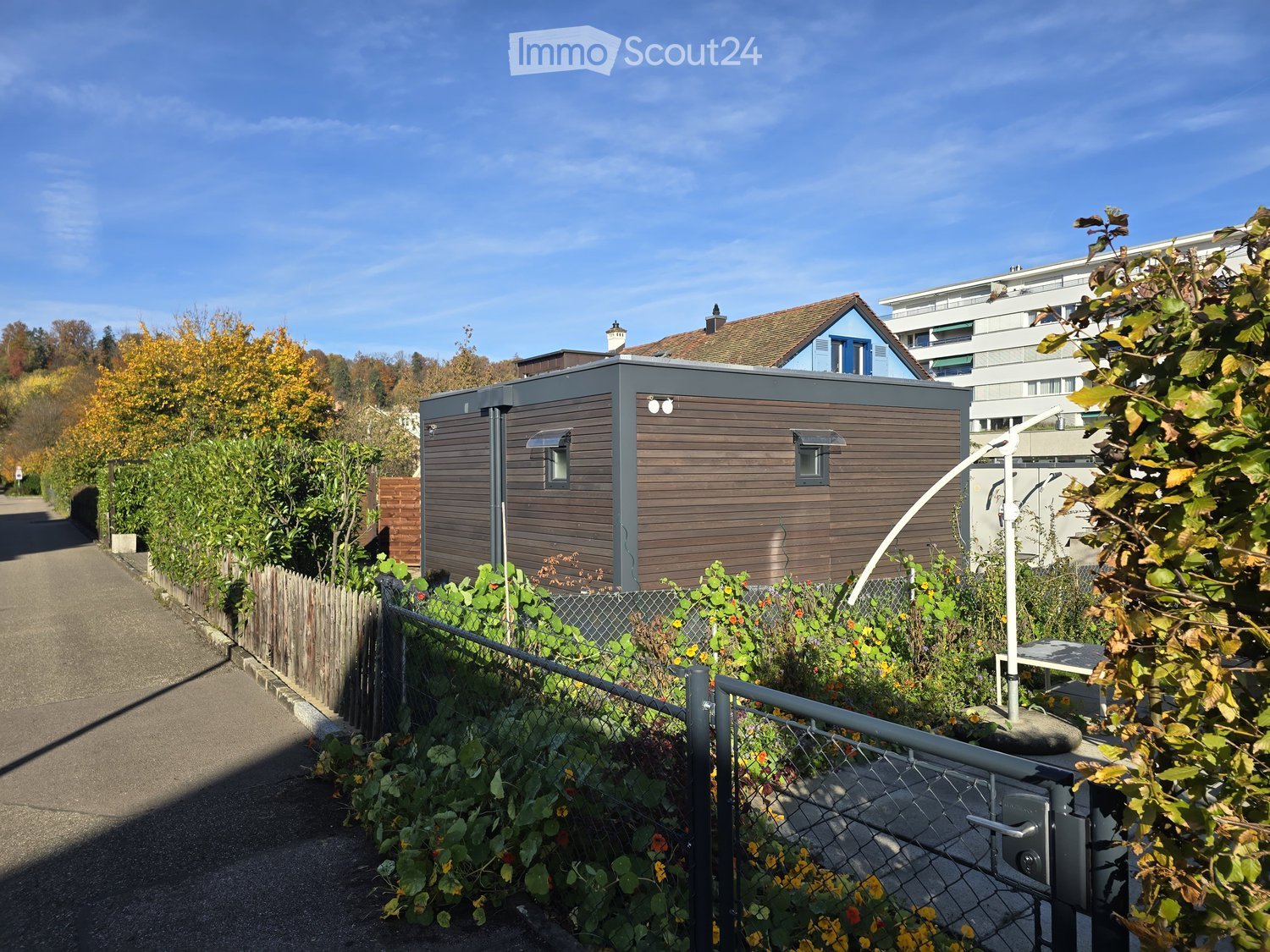 Tiny house, grey and brown exterior, two windows, fenced area with gate