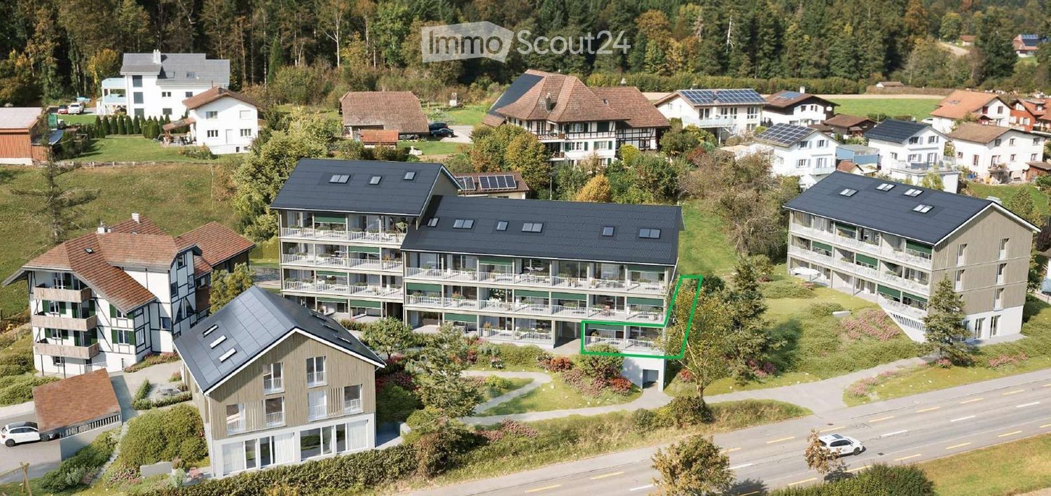 2-story apartment complex with balconies and solar panels, located on a hill overlooking a road and greenery.