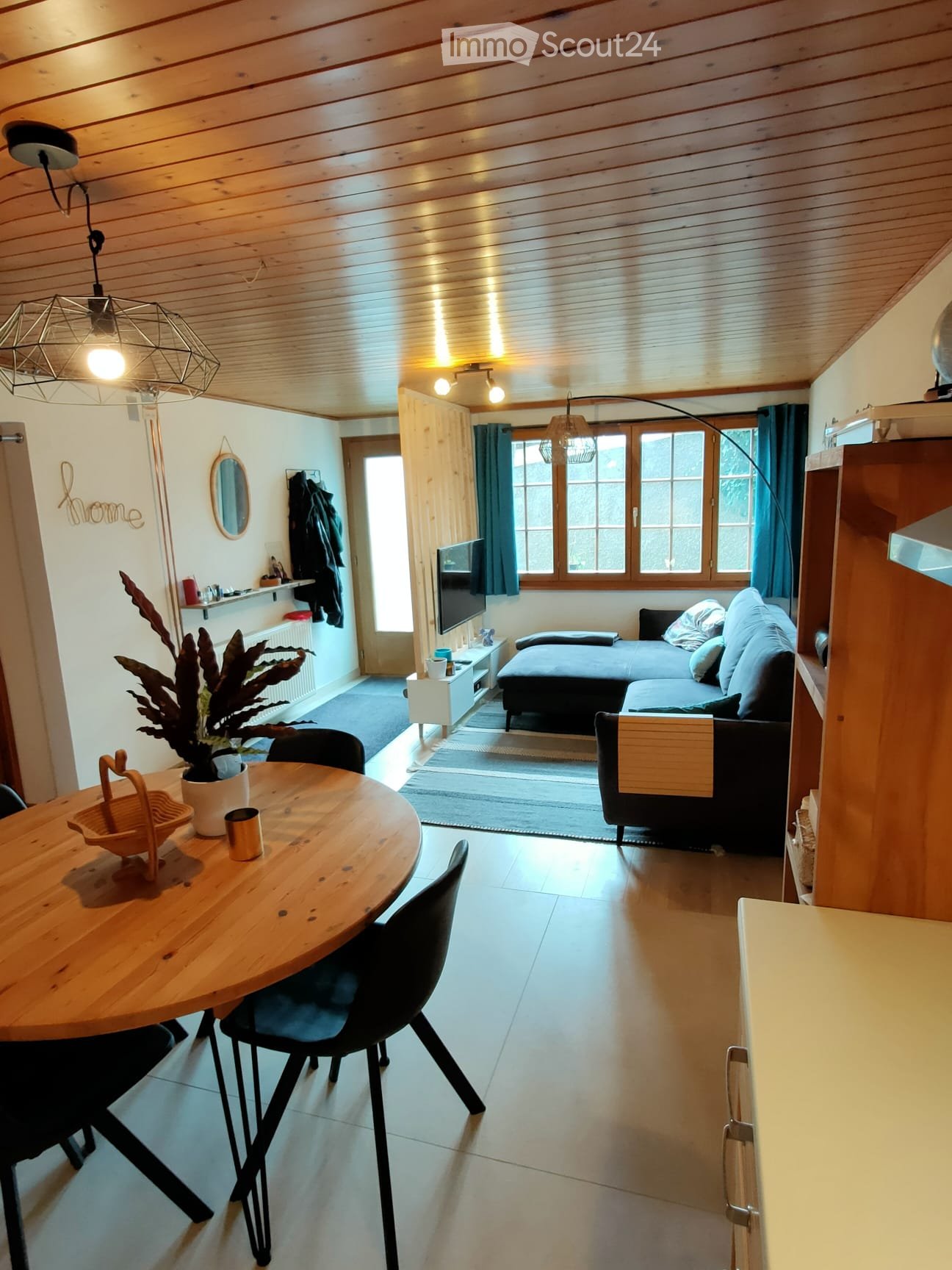 Living room with wooden table, chairs, a sofa with pillows, a television, a shelf, and a lamp