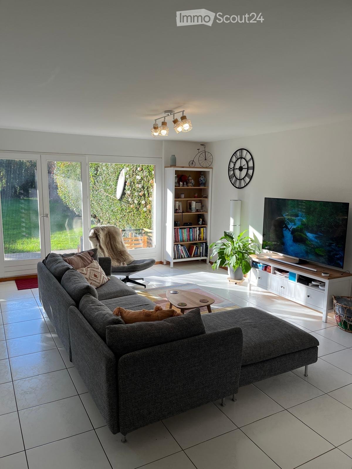 large windows, sliding doors leading to a balcony, couch, armchair, bookshelf, television