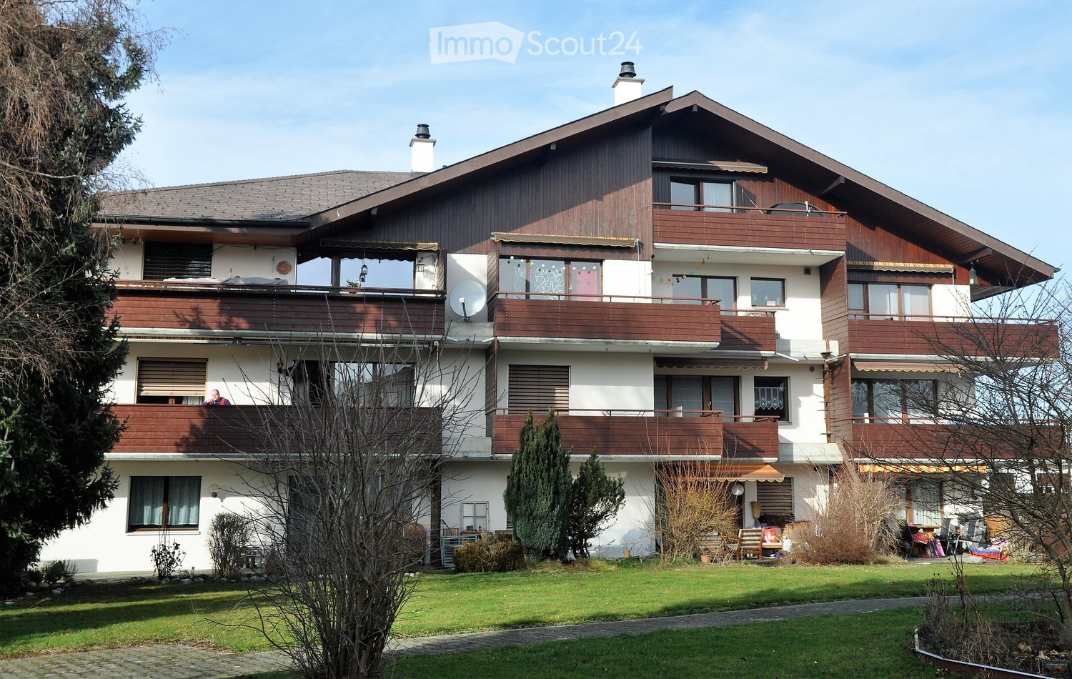 3 story building, brown wooden accents, multiple balconies, satellite dish, green roof