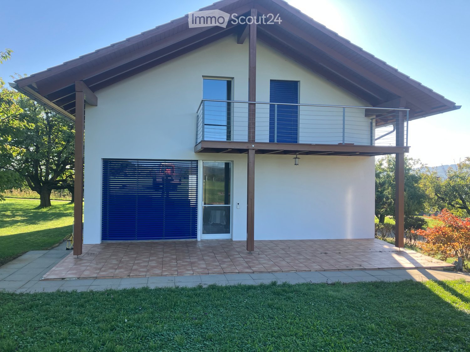 modern house, white exterior, brown roof, blue garage door, balcony, paved terrace