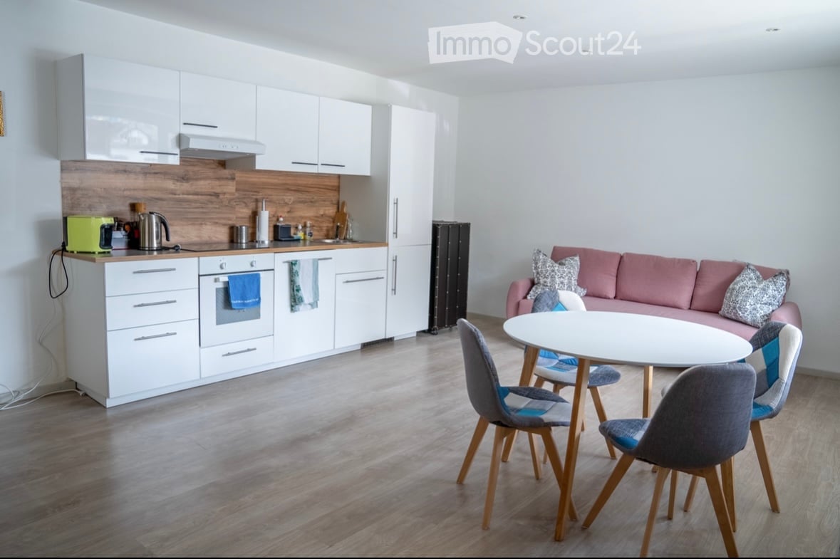 white wooden cabinets, kitchen appliances, wooden floor, pink sofa, dining table, chairs
