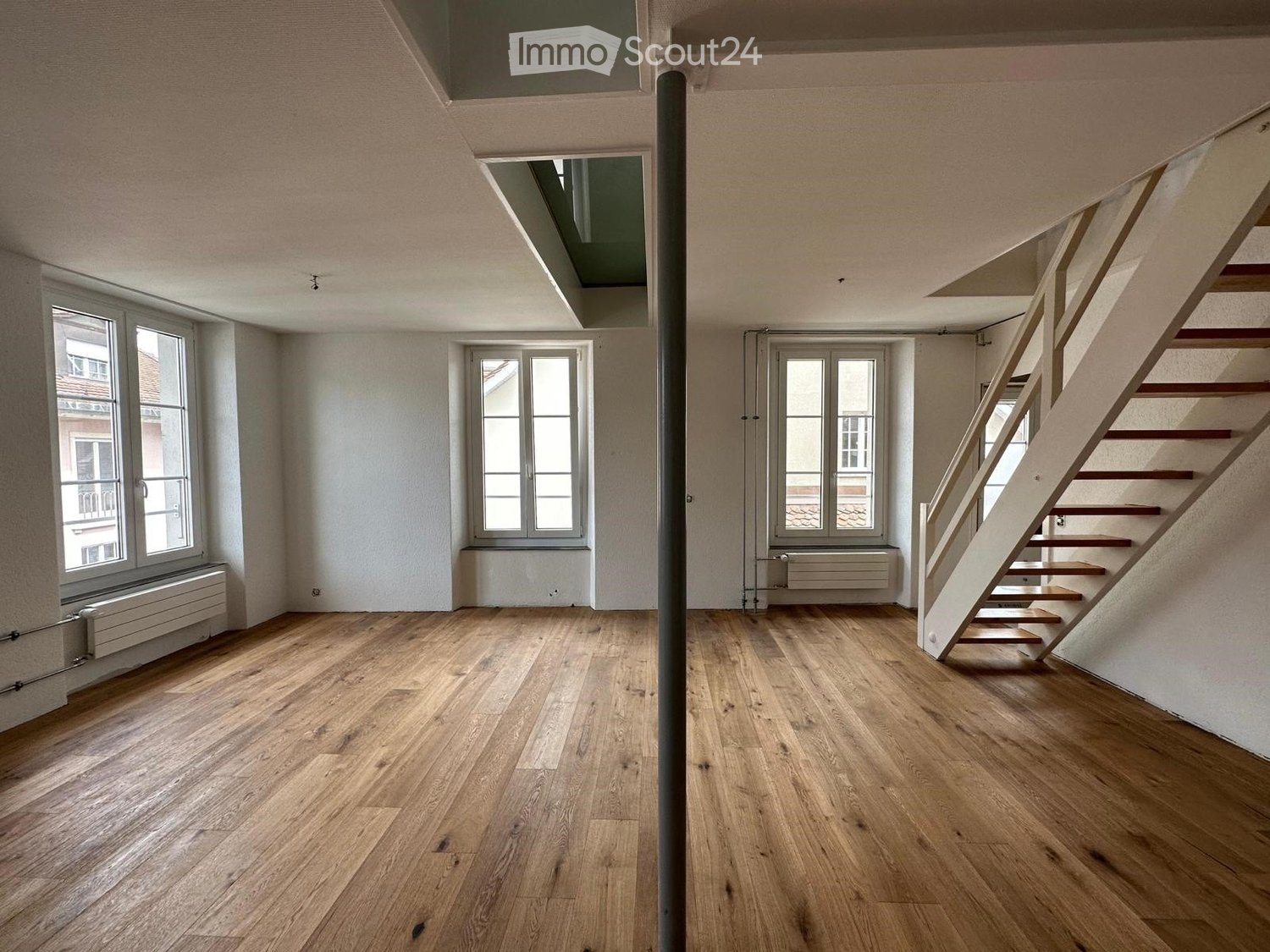 empty room with hardwood floors, white walls, three windows, ceiling pipe, wooden staircase