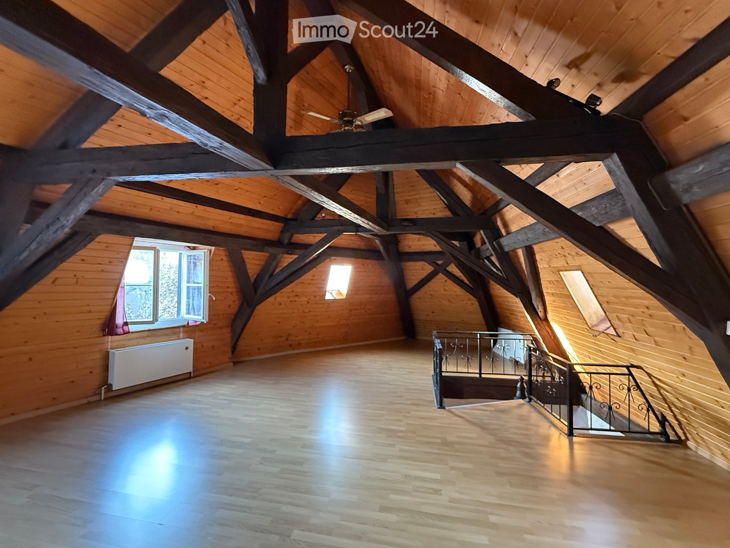 empty attic room, wooden beams ceiling, two windows, ceiling fan, wooden flooring, metal railing