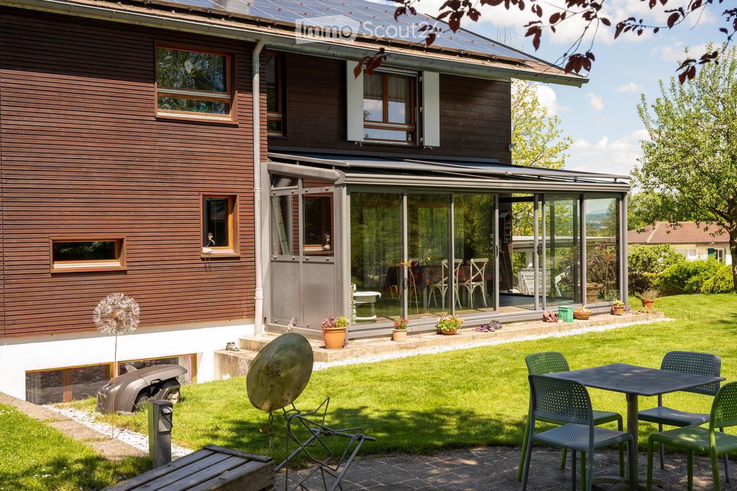 House: Wooden exterior, solar panels, glass conservatory, outdoor dining area, garden, charging station