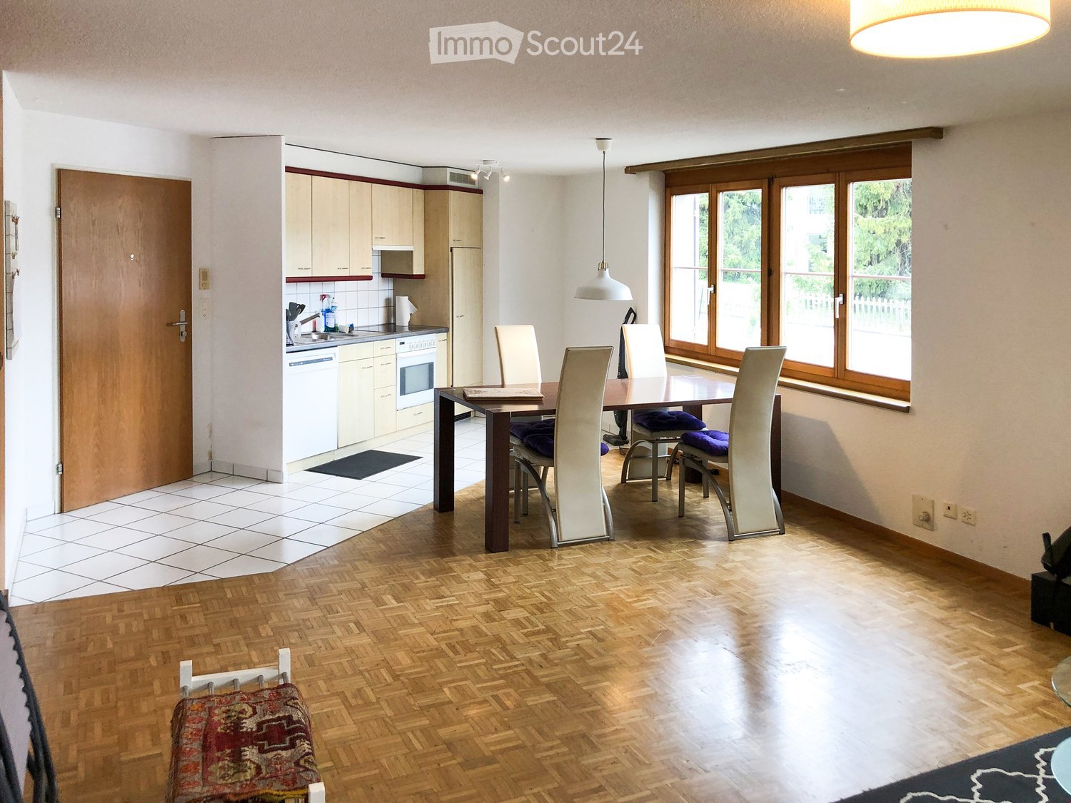 Dining room with table and chairs, wooden floors, white walls, large window, modern kitchen