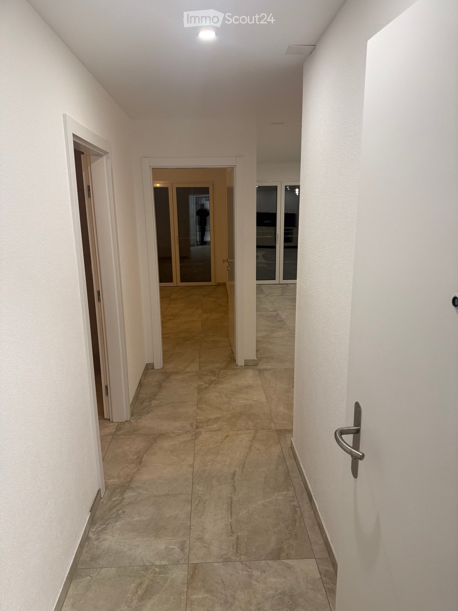 White walls, wooden floors, two doors, empty hallway.