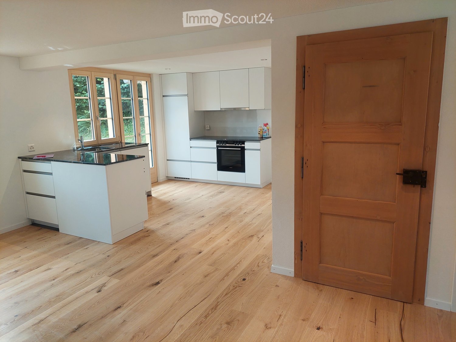 a modern kitchen with an island, white cabinets, wooden floors, and open space