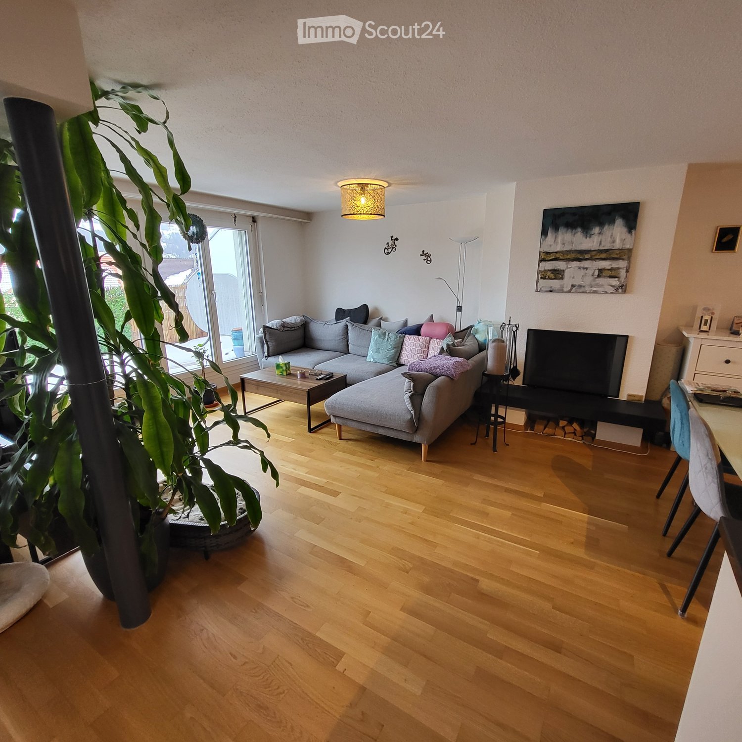 living room with sectional sofa, hardwood floors, large window, couch, coffee table, lamps, artwork, potted plants, fireplace