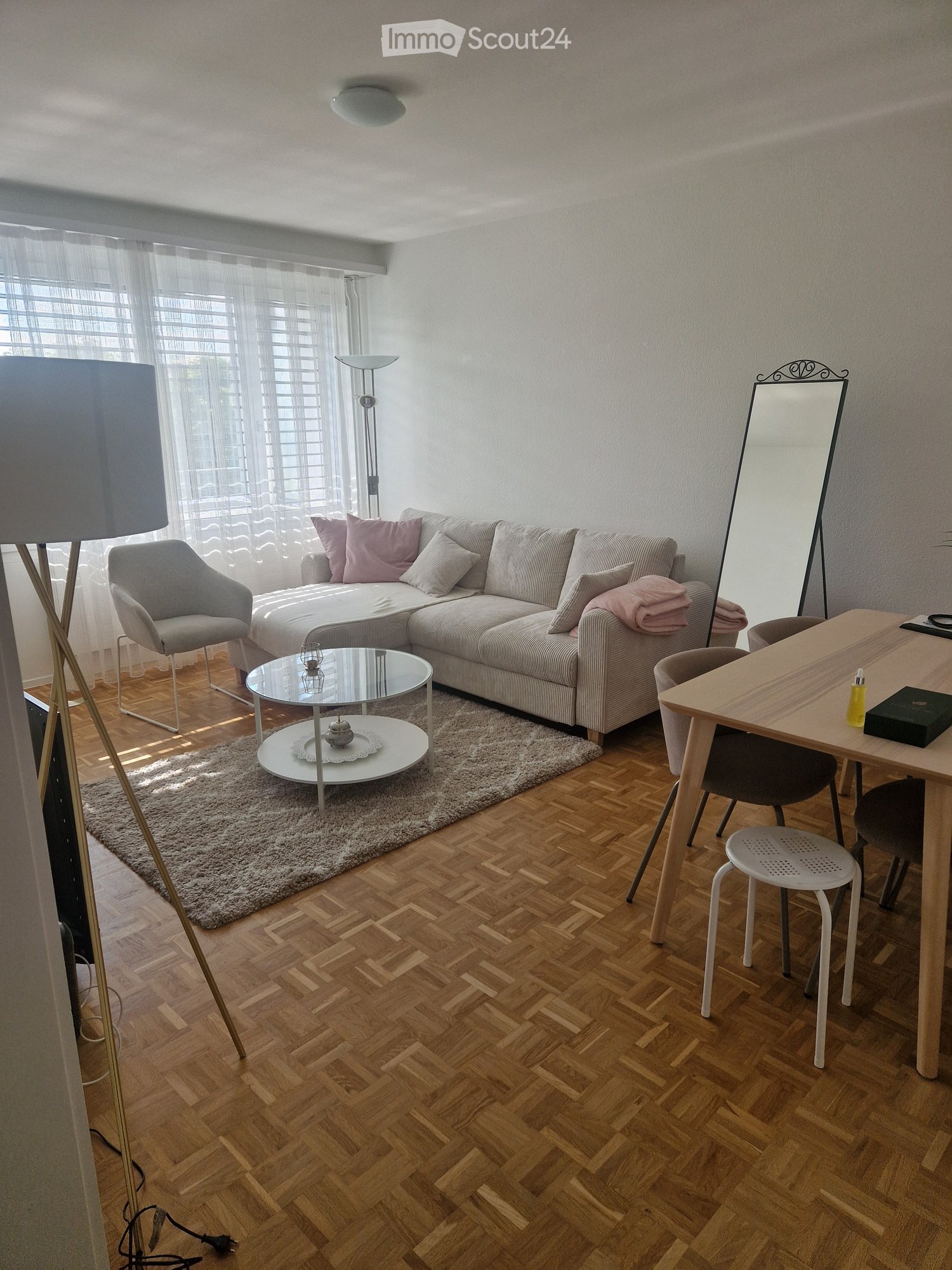 white walls, parquet floor, grey sofa, coffee table, lamp, chair, mirror, table with chairs