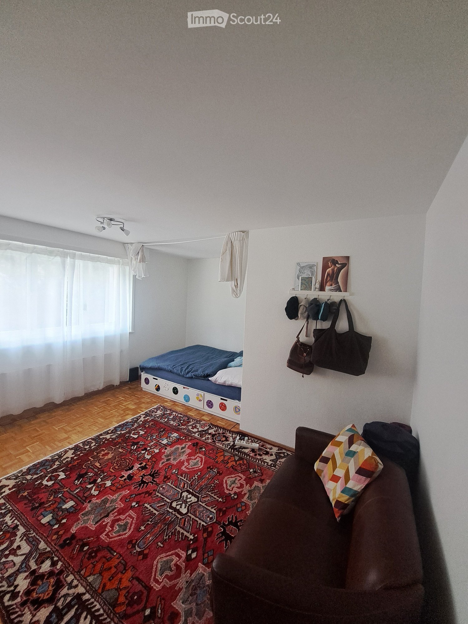 bed, carpet, bed sheet, bed pillow, sofa, pillow, window with curtain, lamps, shelves with pictures and hats