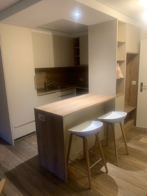 Counter, stools, cabinets, wooden floor, sink with faucet, refrigerator