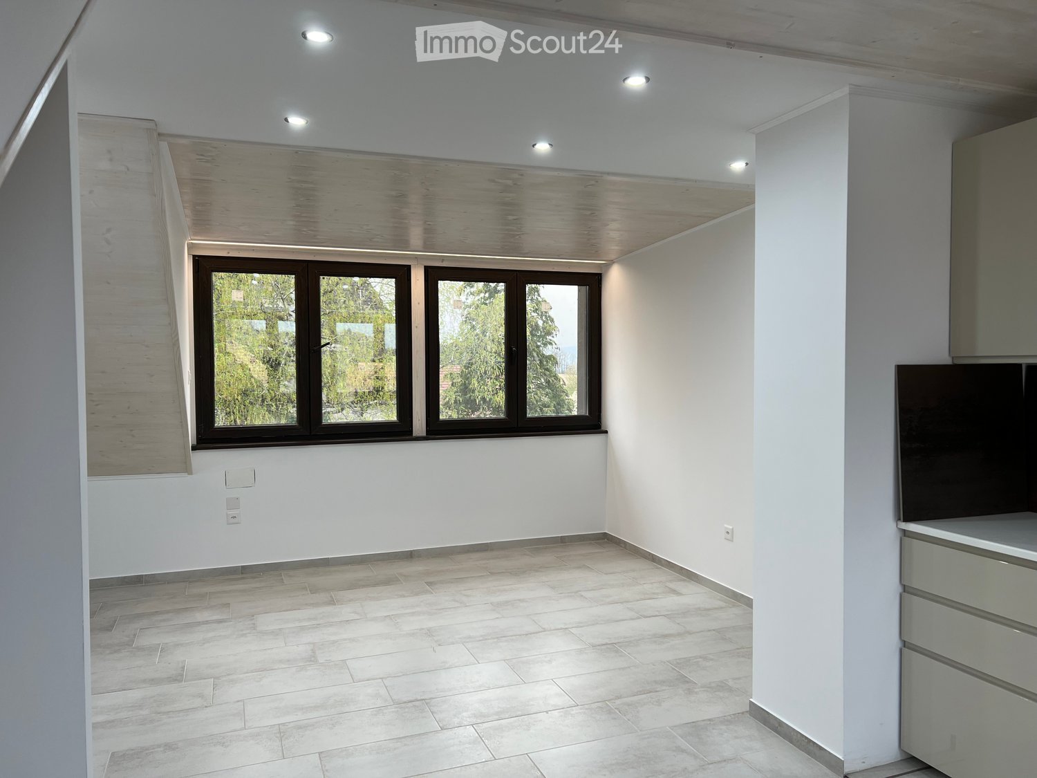 Empty room, white walls, tiled flooring, three windows with dark frames, recessed lighting on the ceiling