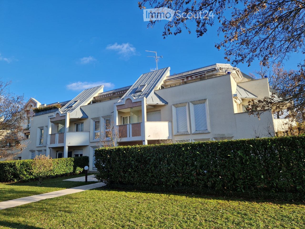 White multistory building, multiple balconies, landscaped front yard with hedge and grass