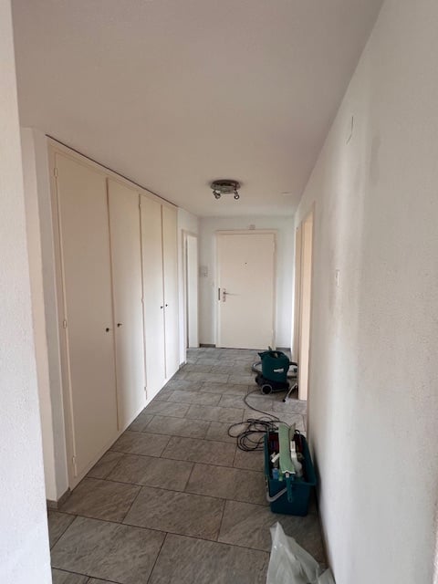 Empty hallway, tiled floor, white walls, cabinets, door, vacuum cleaner, storage boxes.