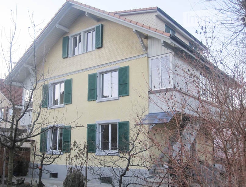 yellow two-story house, tiled roof, green shutters, many windows, balcony