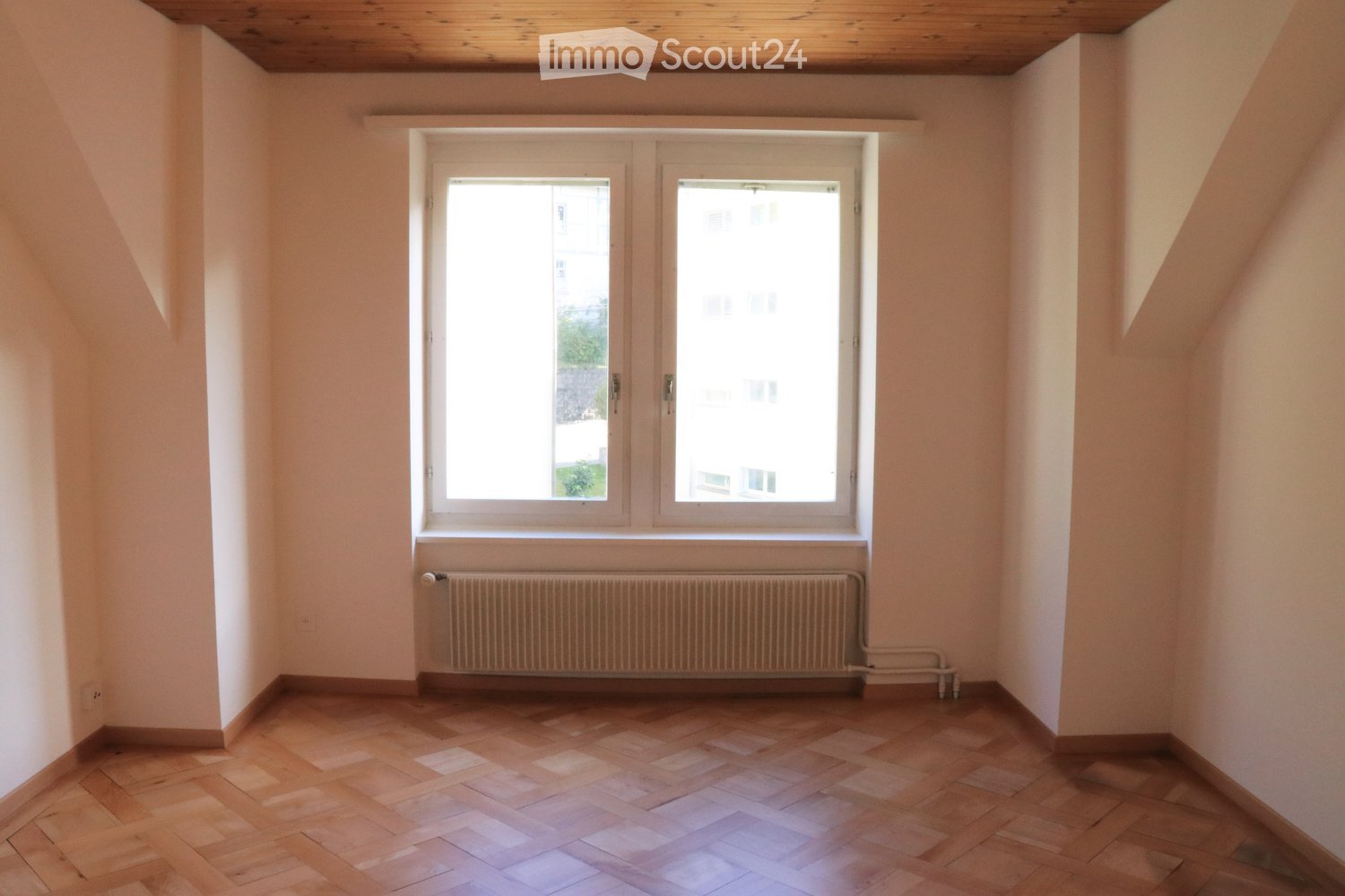 Empty room with parquet floor, white walls, a large window and a white radiator