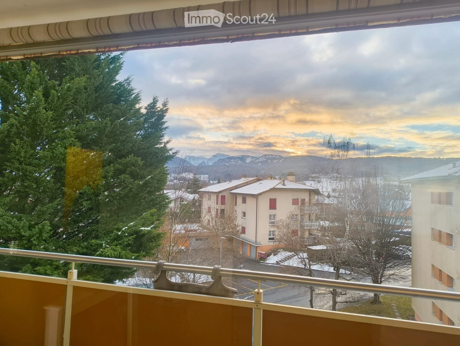 Balcony view of snowy town, mountains, and trees in distance