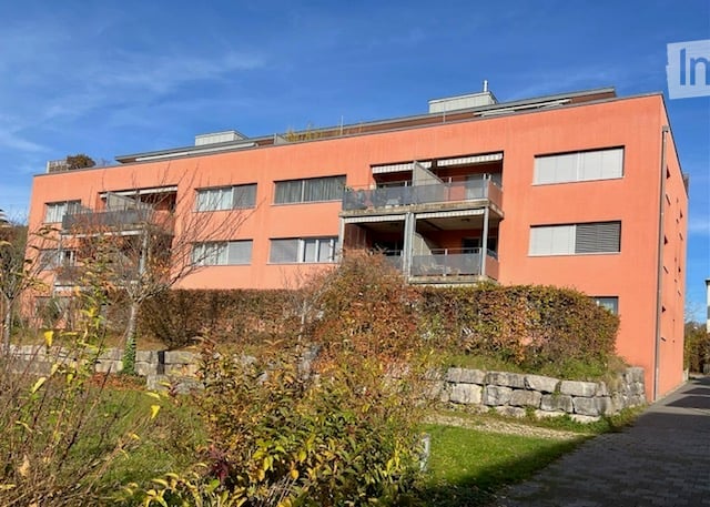 Three-story apartment building with multiple balconies and a red facade.