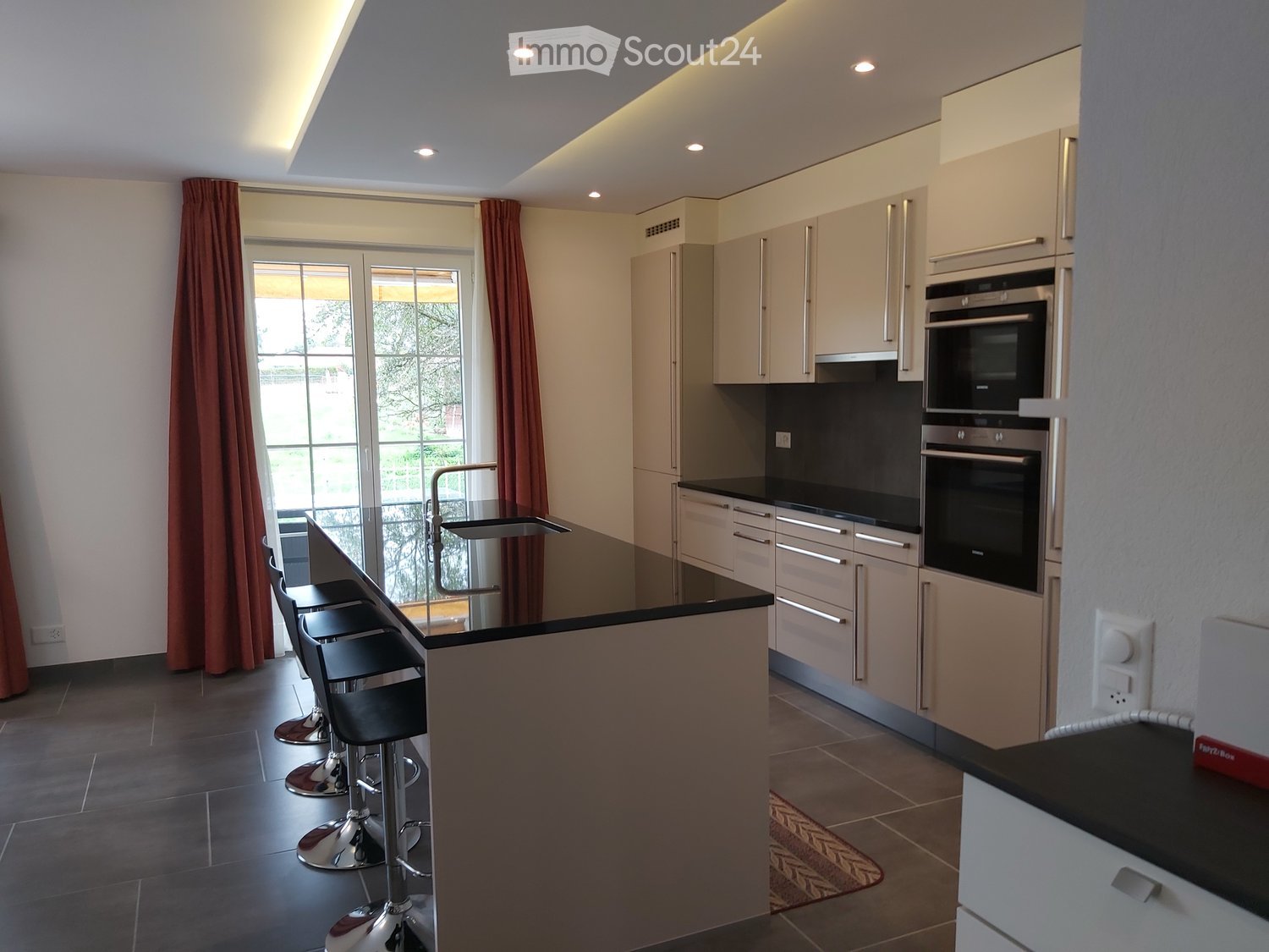 Modern kitchen with bar seating, black countertops, white cabinets, glass windows, stainless steel faucet, built-in oven, and microwave.