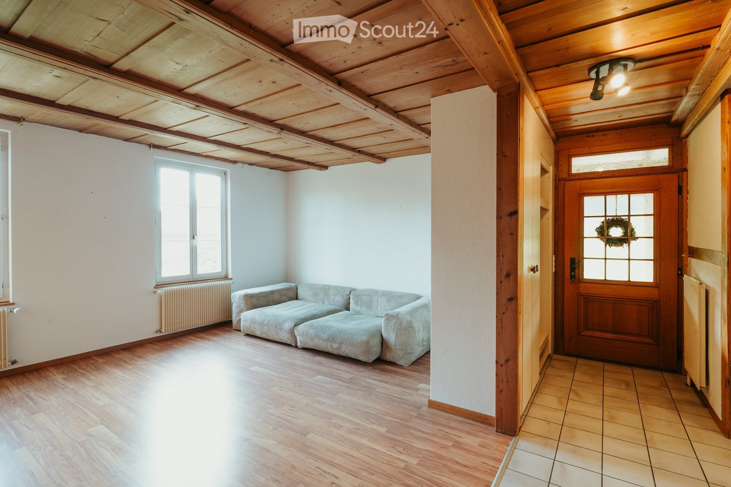 living room, large couch, large window, wooden ceiling, wooden floor, radiators
