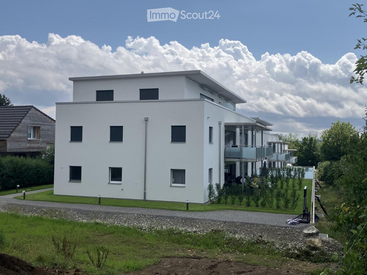 2 story modern house, white exterior, glass windows, balconies, driveway, garden, trees, cloudy sky