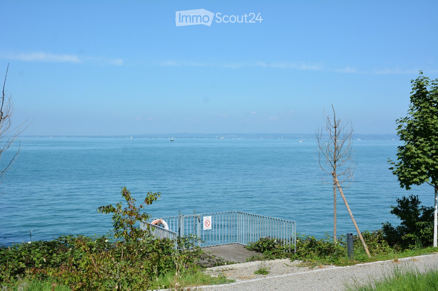 large body of water, boat in distance, railings, trees, plants, sign