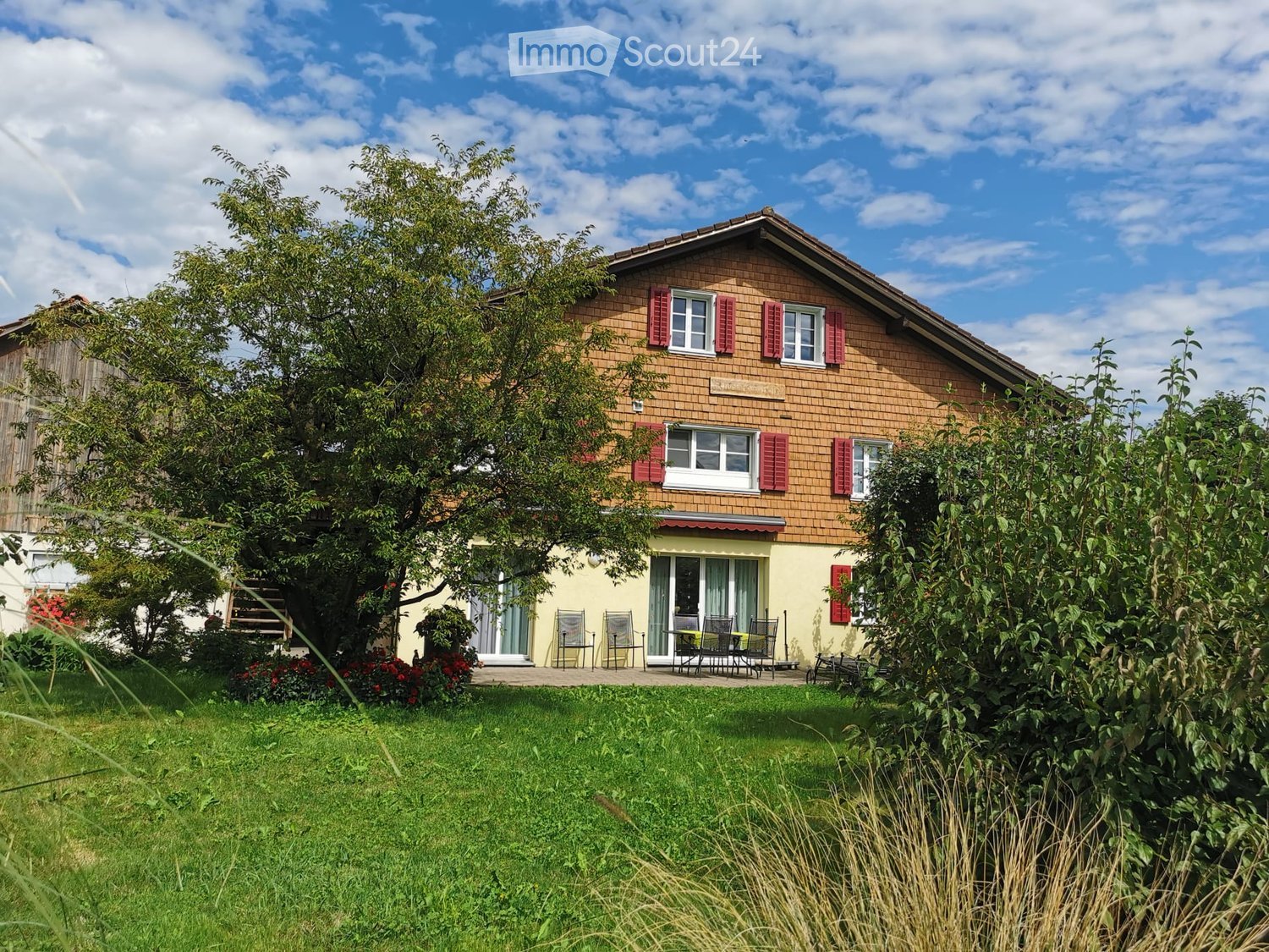 2 story house, brown brick, red shutters, large tree, outdoor seating, garden
