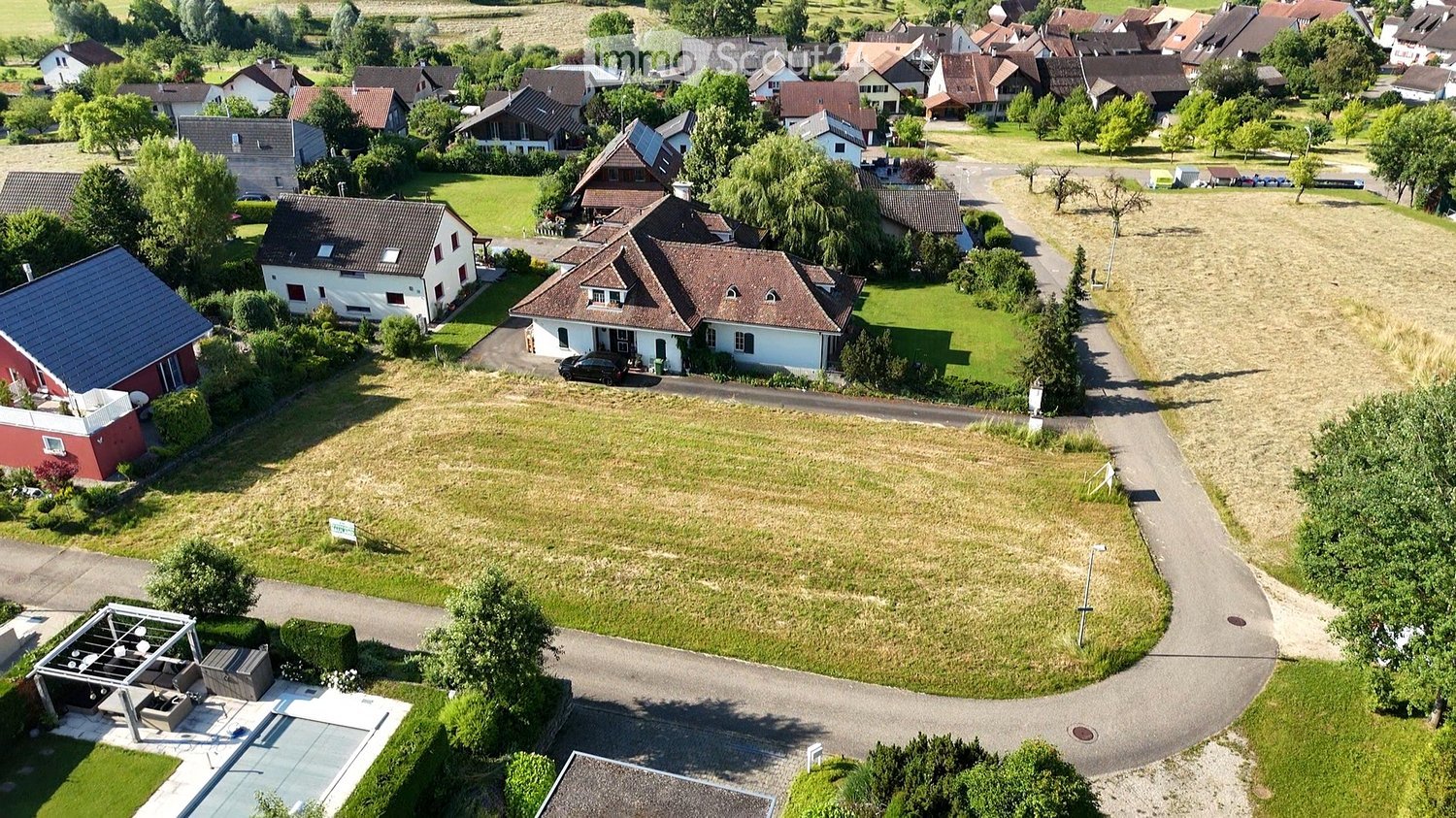 Single-family house, brown roof, white walls, cars parked on driveway, surrounded by trees and greenery.