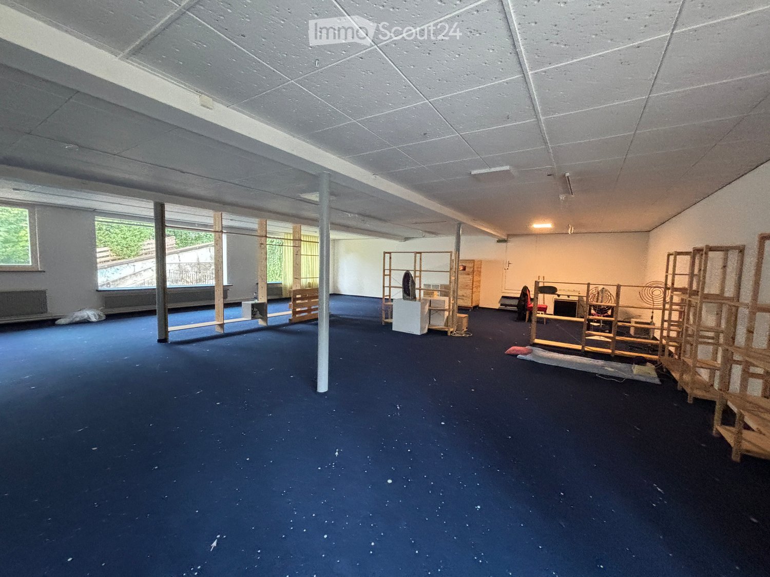 wide, open space, blue flooring, high ceilings, large windows, shelves, various objects and equipment