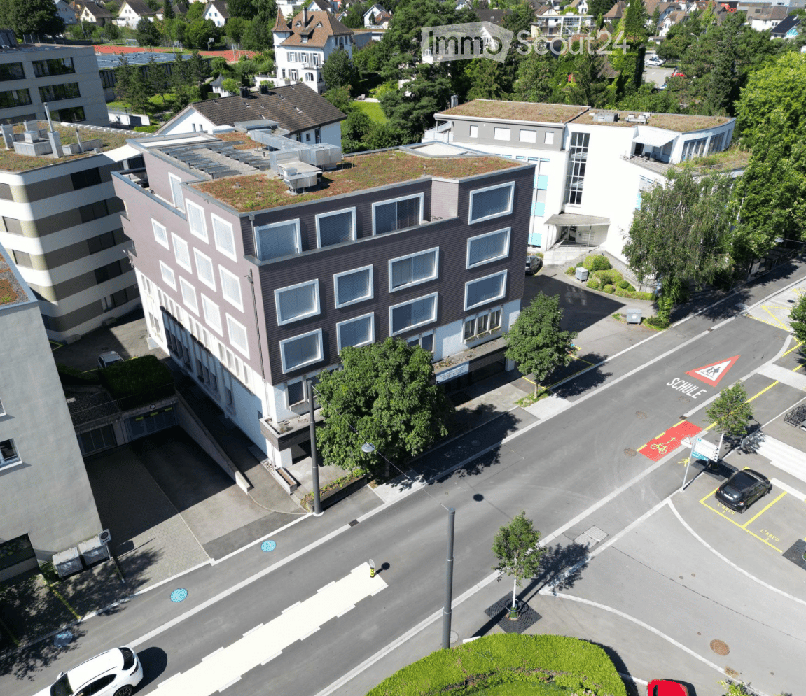 Aerial view of a multi-story building with several windows, a green roof, and an underground parking entrance.