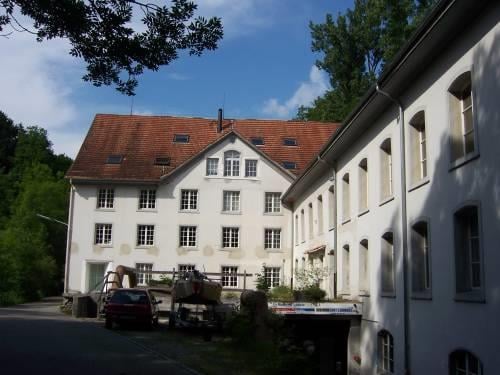 large white building with multiple windows, brown roof, driveway, parked car, trailer