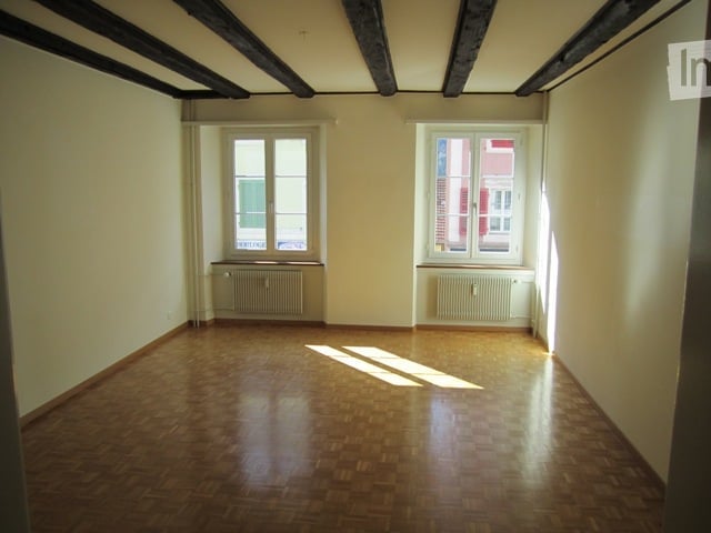 empty room, wooden floor, two windows, radiators, wooden beams on ceiling