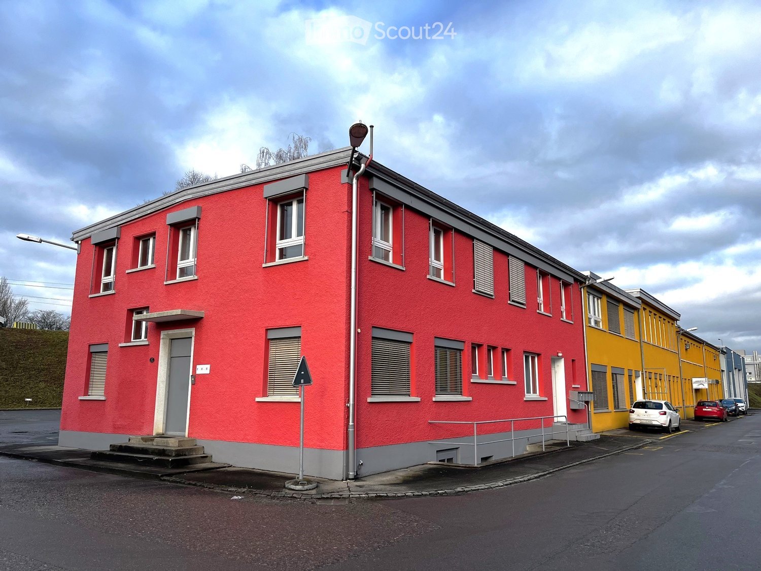 3 story house, red and grey paint, multiple windows, door at the center, cars parked next to it