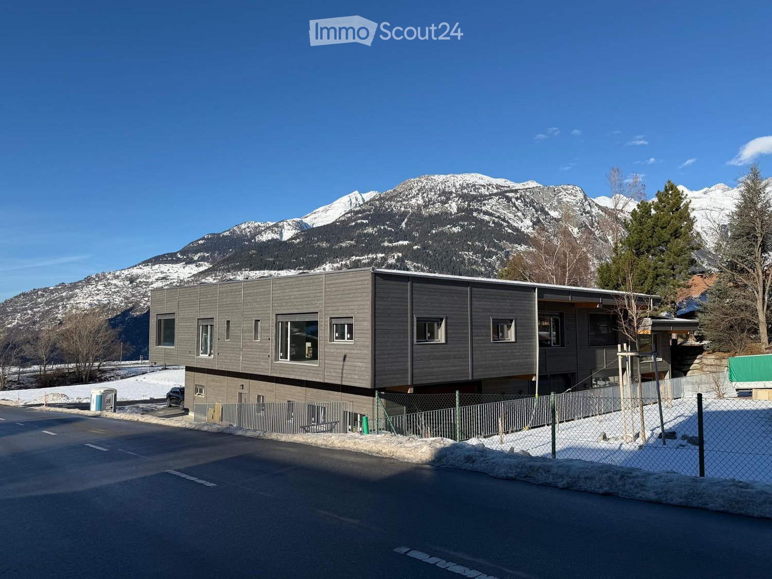 Modern house, multiple windows, surrounded by snow, mountains in the background