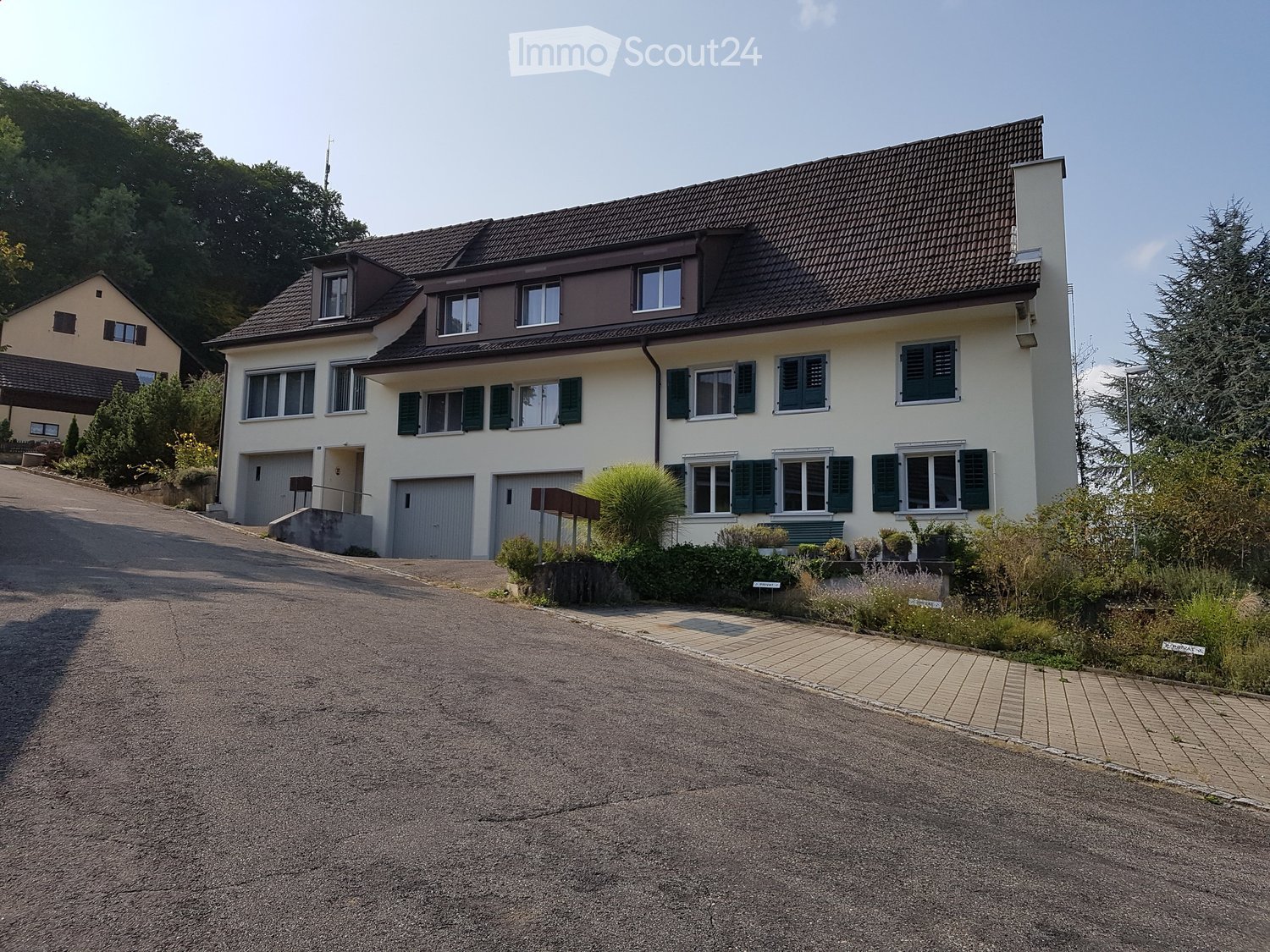White house with brown roof, 3 floors, 2 garages on the ground floor, located at the end of a road, large windows