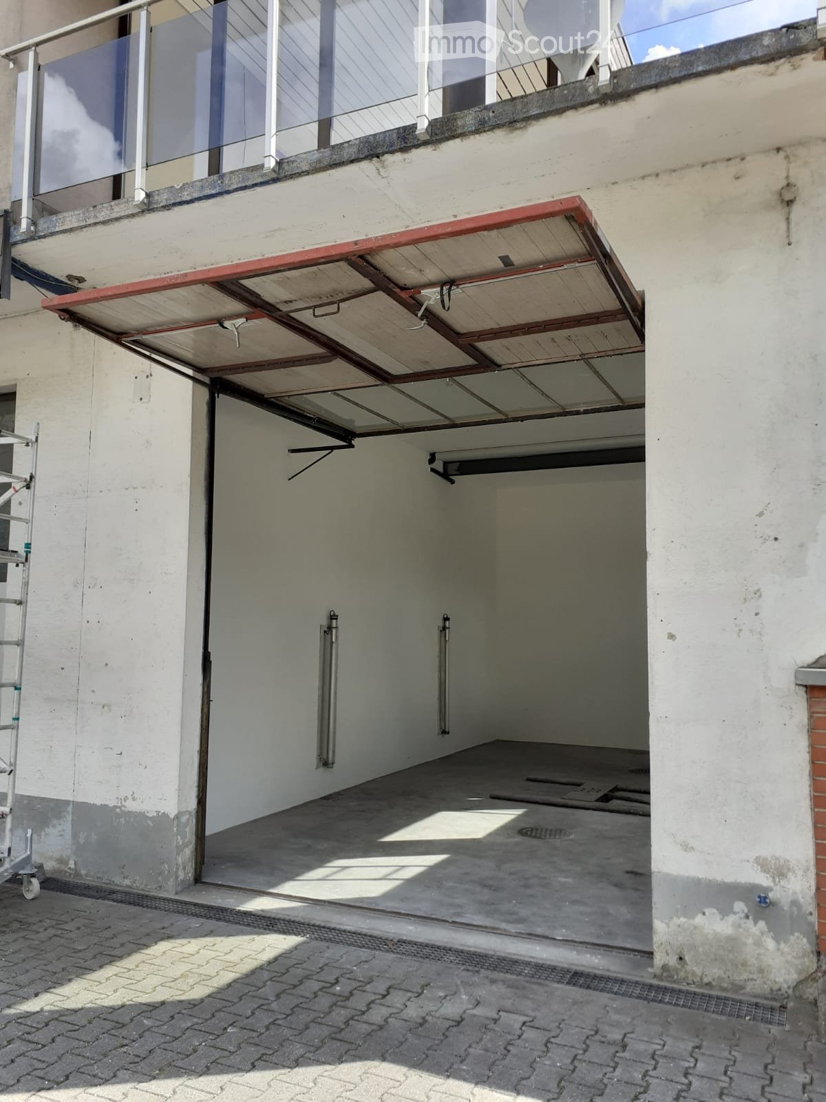 Garage with a retractable roof, concrete floor, and white walls. The roof is partially open, revealing the sky above.