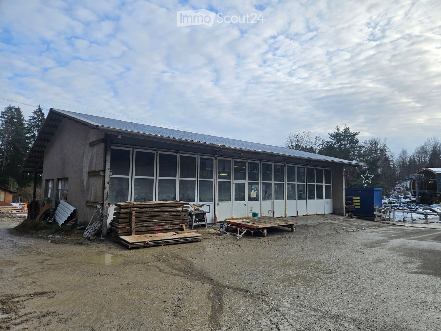 industrial building with glass windows, large wooden doors, roof, stacks of wooden planks