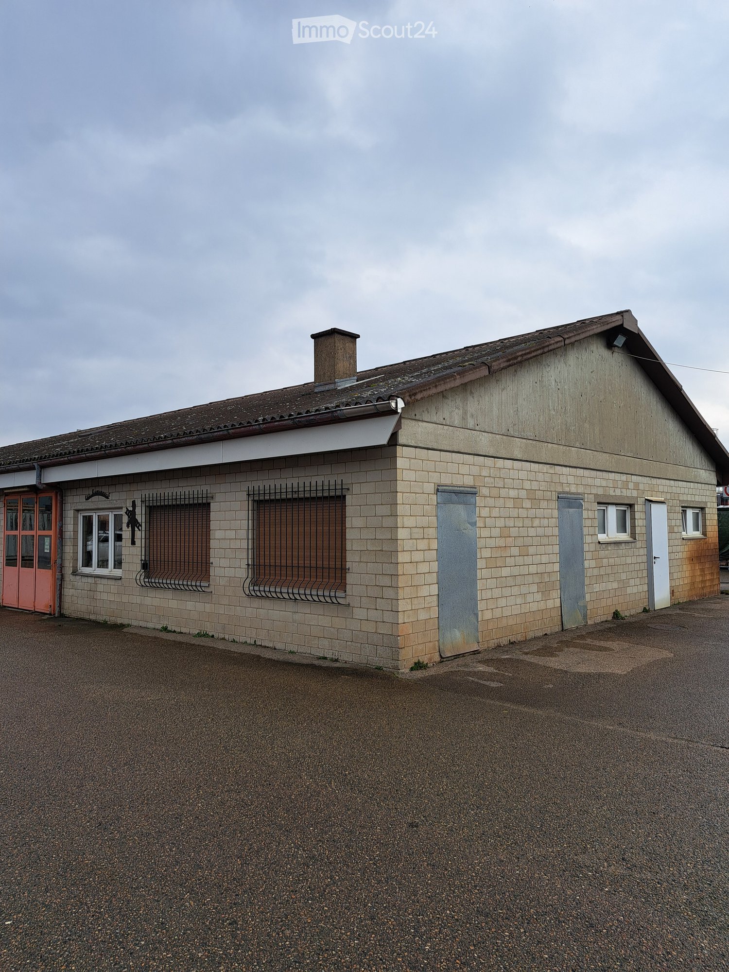 Industrial building with brick walls, a brown roof, large windows, red entrance door, metal shutters, metal doors, and chimney
