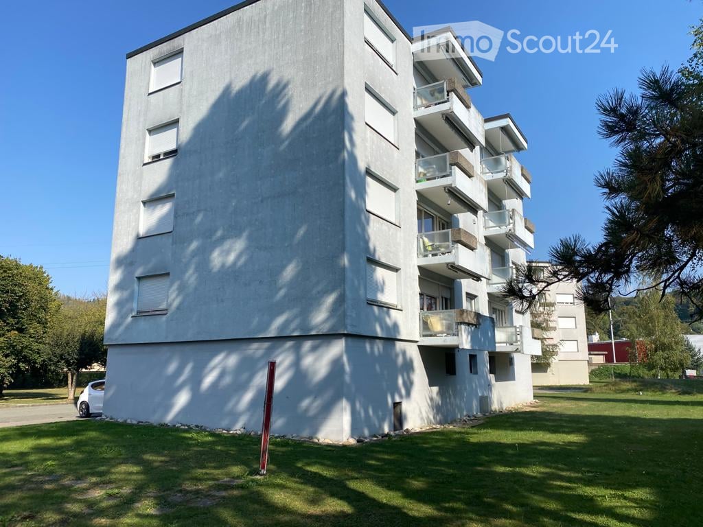 Concrete building, multiple balconies, white exterior, several floors, modern design, cars parked nearby, greenery
