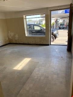 Empty room with tiled floor, wall damage, glass door and window, view of street and car.