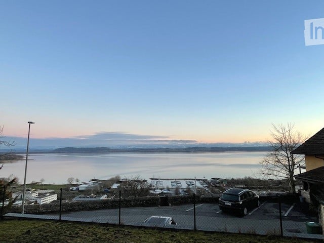 House with water view, 2 cars parked in a parking lot, trees, mountains