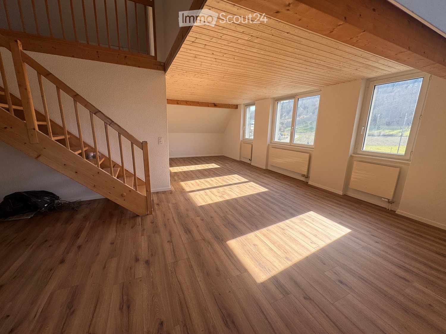 Spacious room, wooden floors, wooden ceiling, three large windows, wooden staircase, radiators, view of a mountain