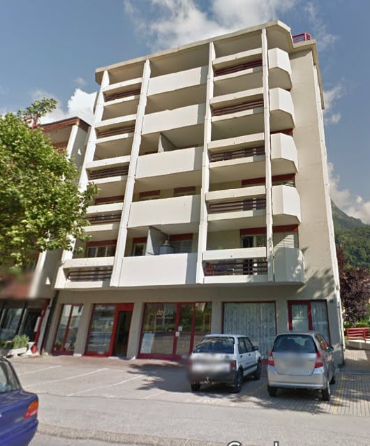 modern multi-story building, balconies, parking area, glass doors, red frames