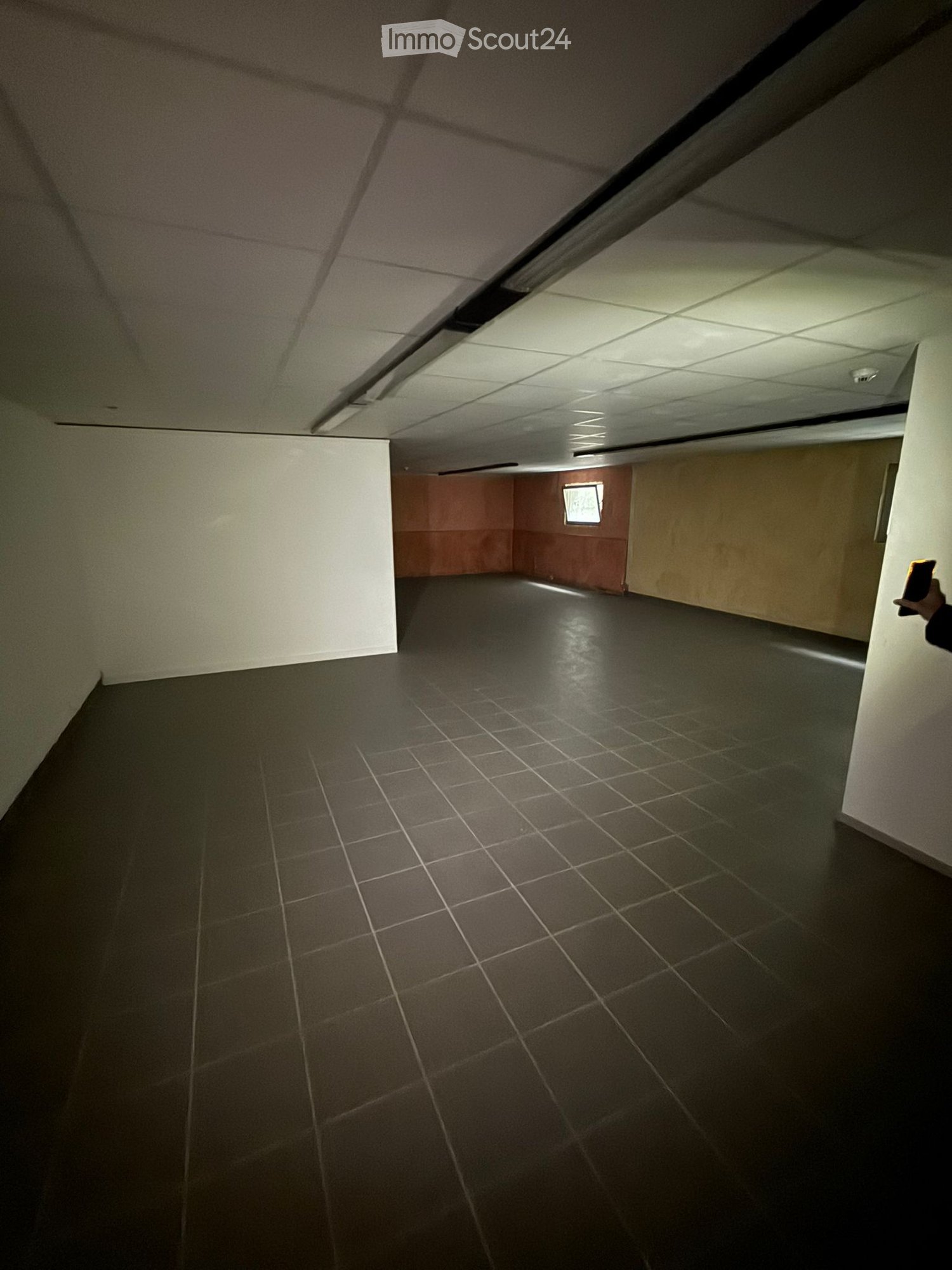 Empty room with tiled floor, square lights on ceiling, wall on the left and back