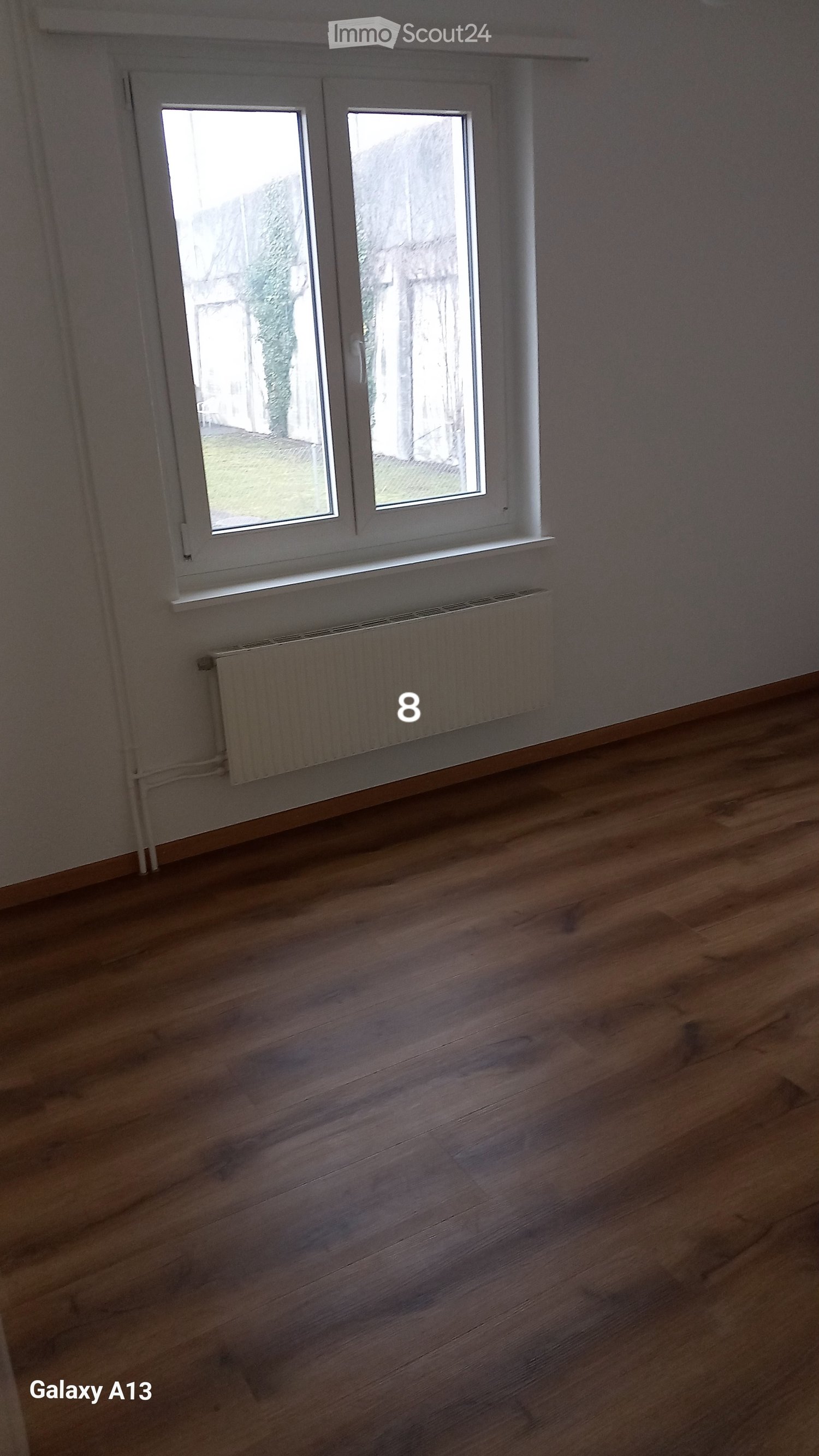 empty room, wooden floor, white wall, white window, white radiator, power outlet on the wall